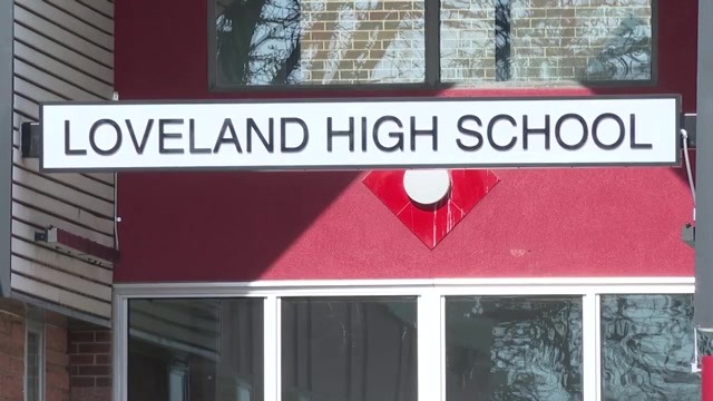 A sign that says "Loveland High School" outside a building with red exterior, white paneling and glass windows