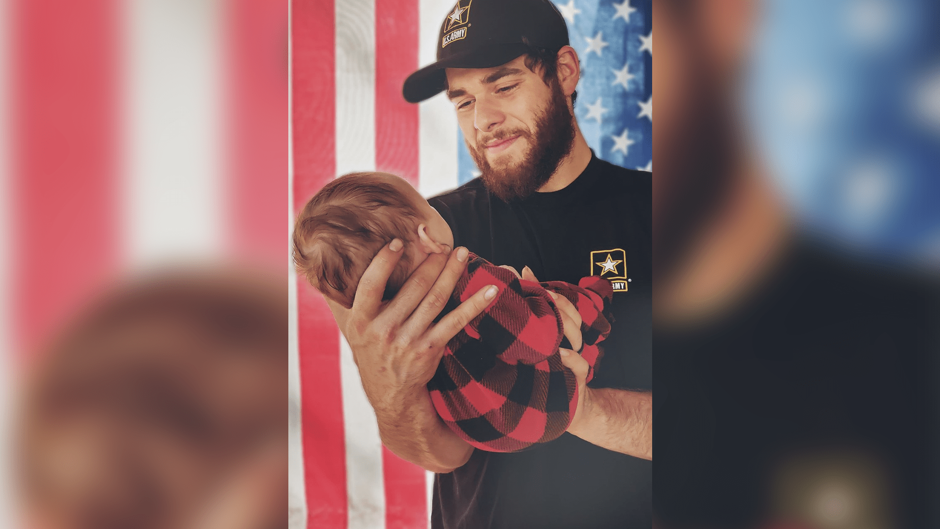 A young man looking down and smiling at a baby he's holding in his arms