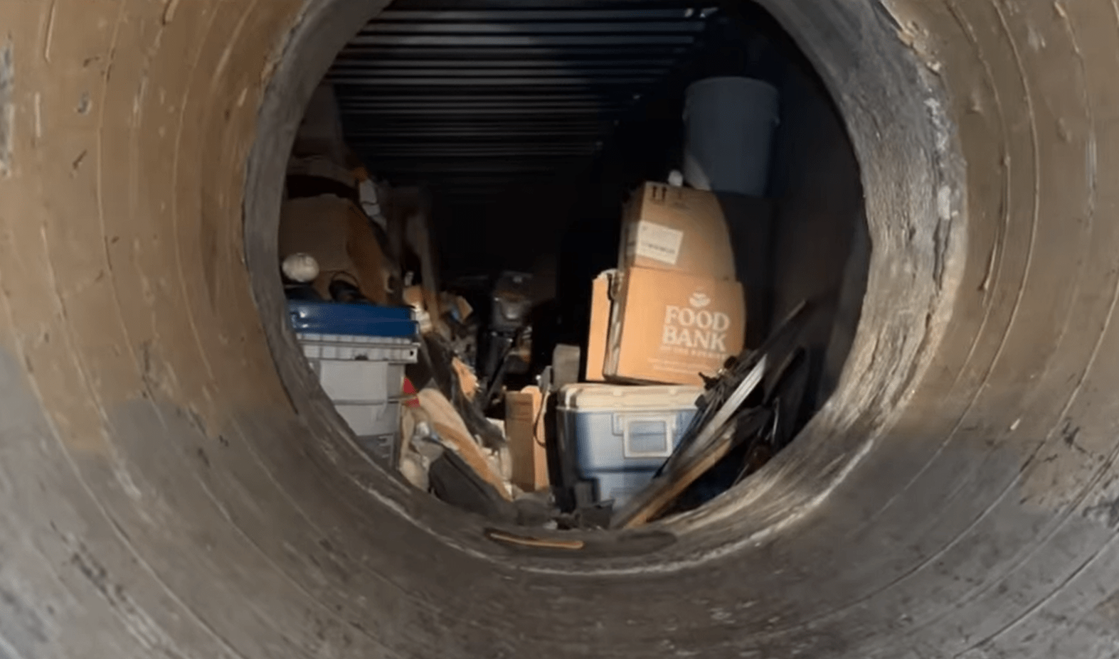 A light shines into a tunnel, showing piles of boxes and clutter