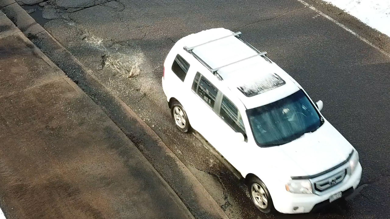 An aerial view of an SUV on a road covered in potholes