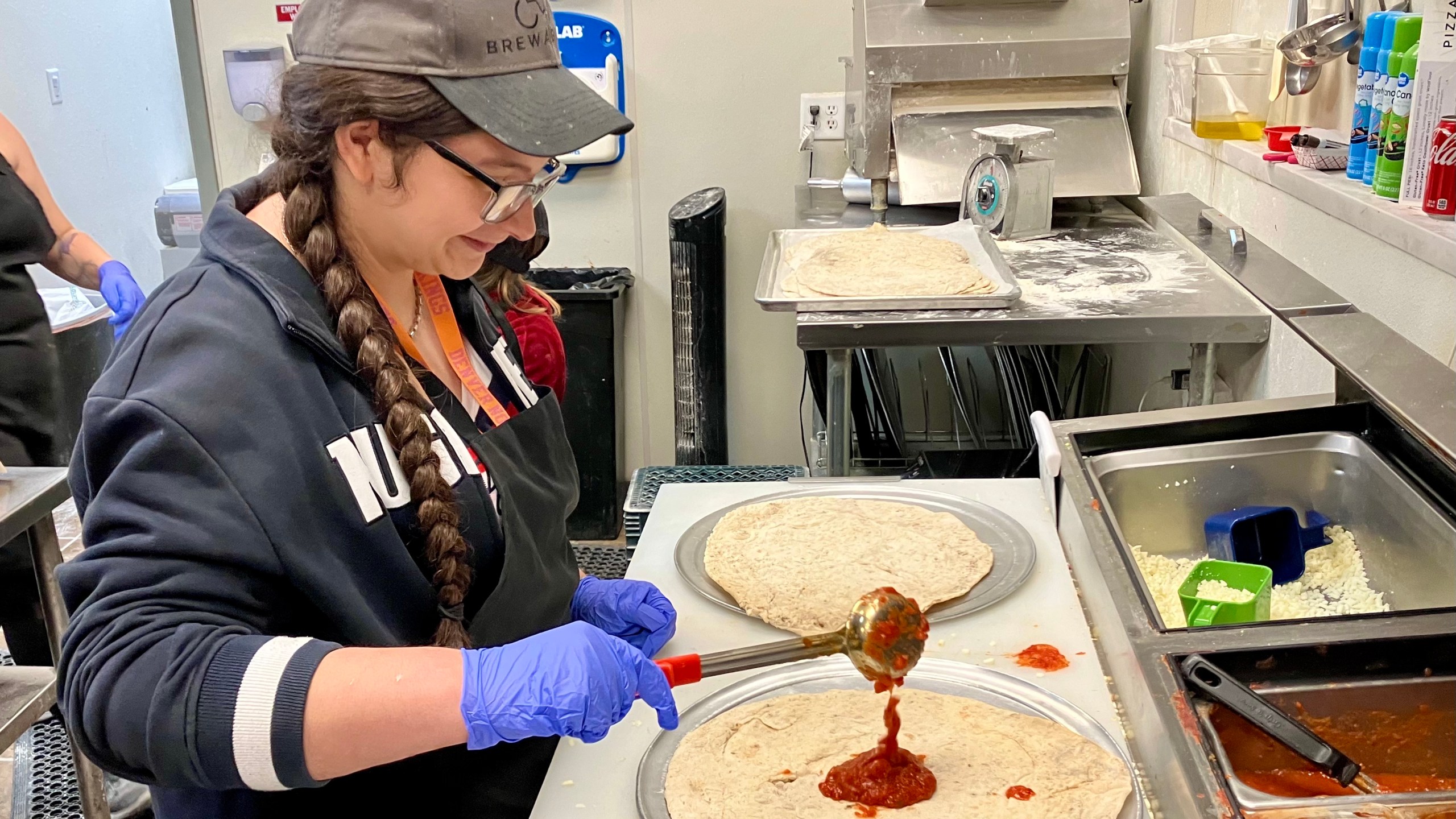 A woman pours sauce on raw pizza dough