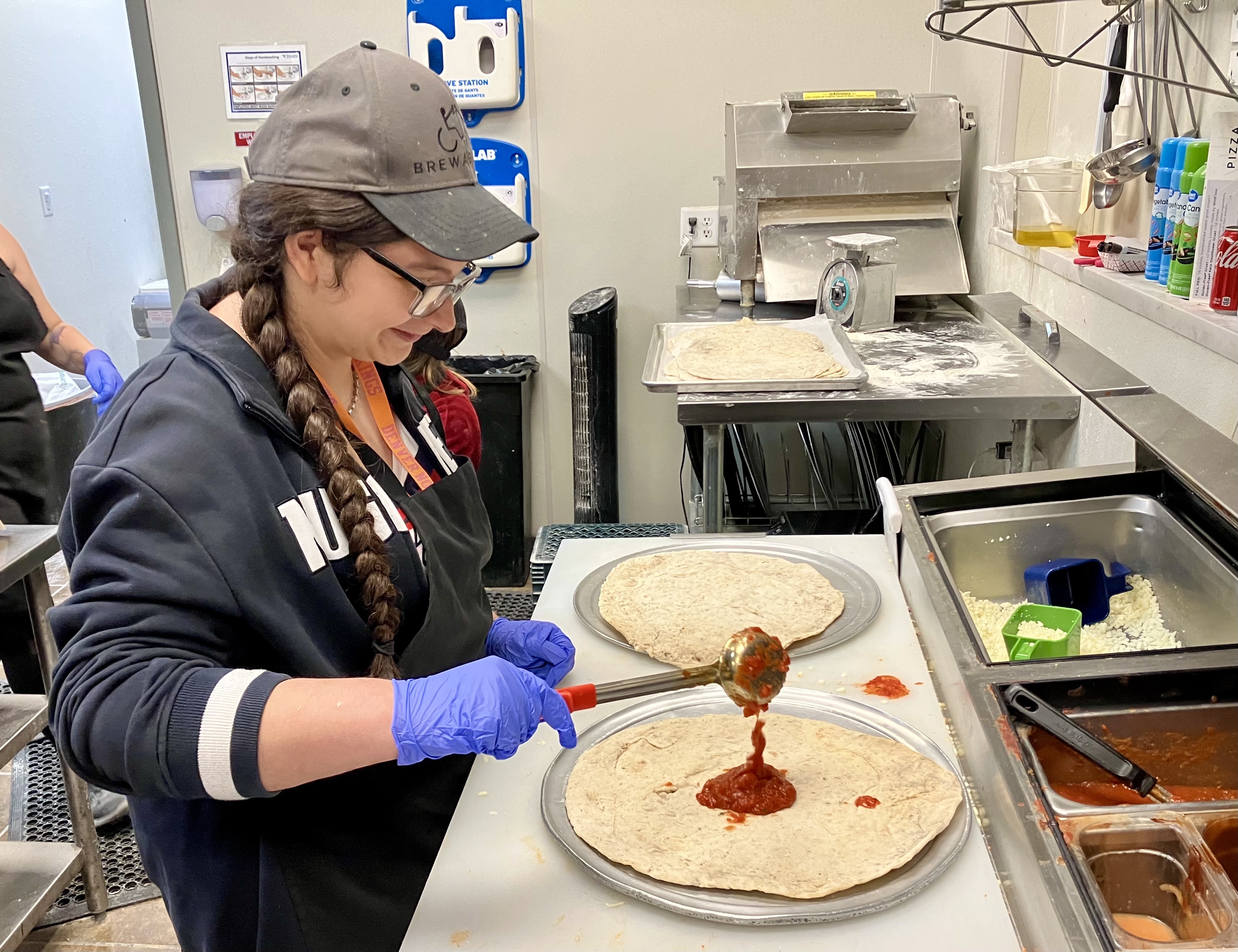 A woman pours sauce on raw pizza dough