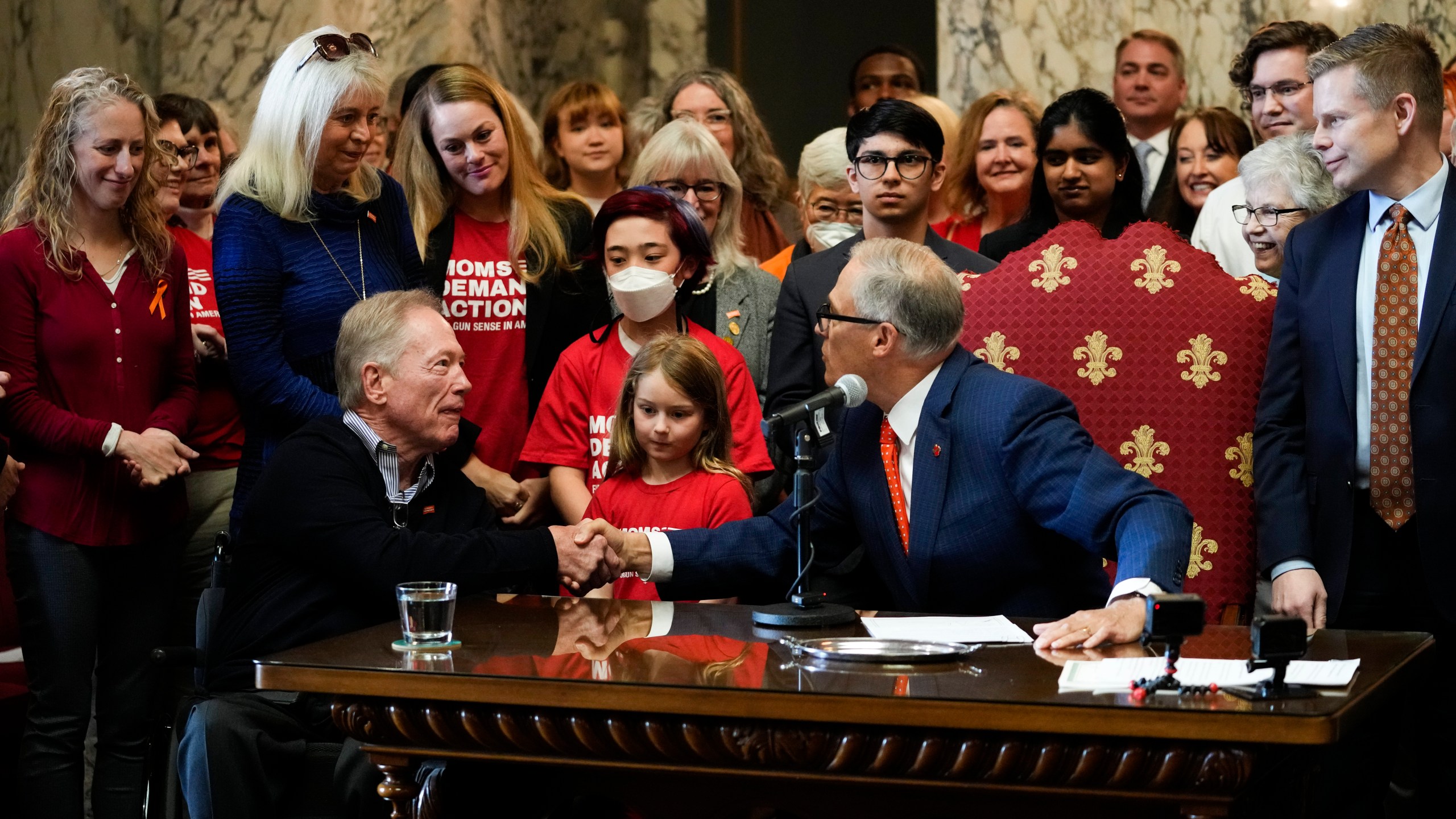 Washington Gov. Jay Inslee shakes the hands of Jim and Ann-Marie Parsons, in blue, whose daughter Carrie was killed in the 2017 Las Vegas shooting, after Inslee signed Senate Bill 5078, which ensures that firearms manufacturers and sellers will face liability if they fail to adopt and implement reasonable controls to prevent sales to dangerous individuals, Tuesday, April 25, 2023, at the Capitol in Olympia, Wash. (AP Photo/Lindsey Wasson)