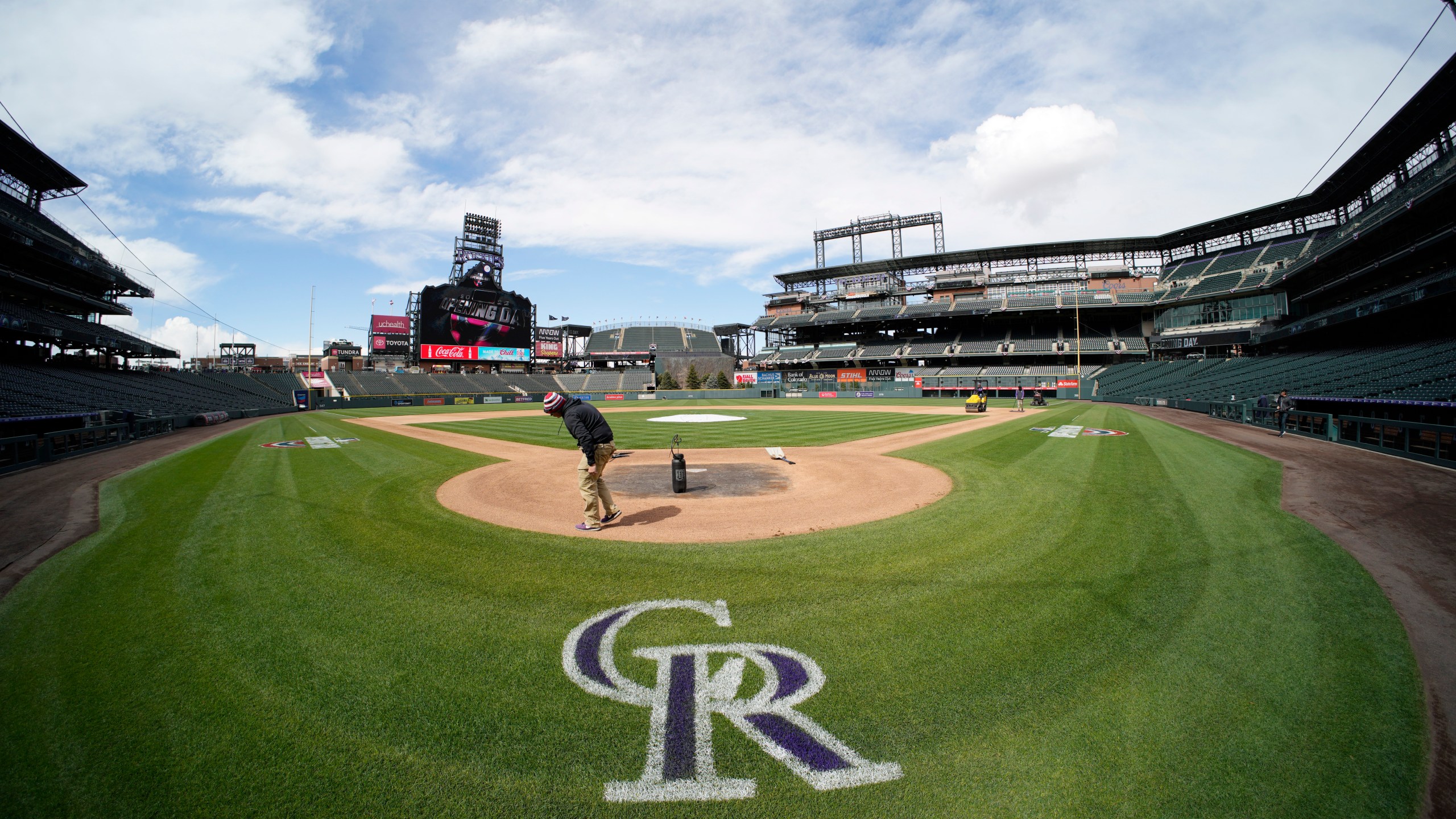 Workers prepare Coors Field on a sunny day with clouds