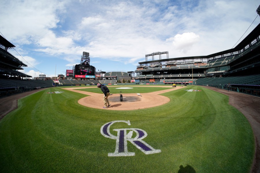 Workers prepare Coors Field on a sunny day with clouds