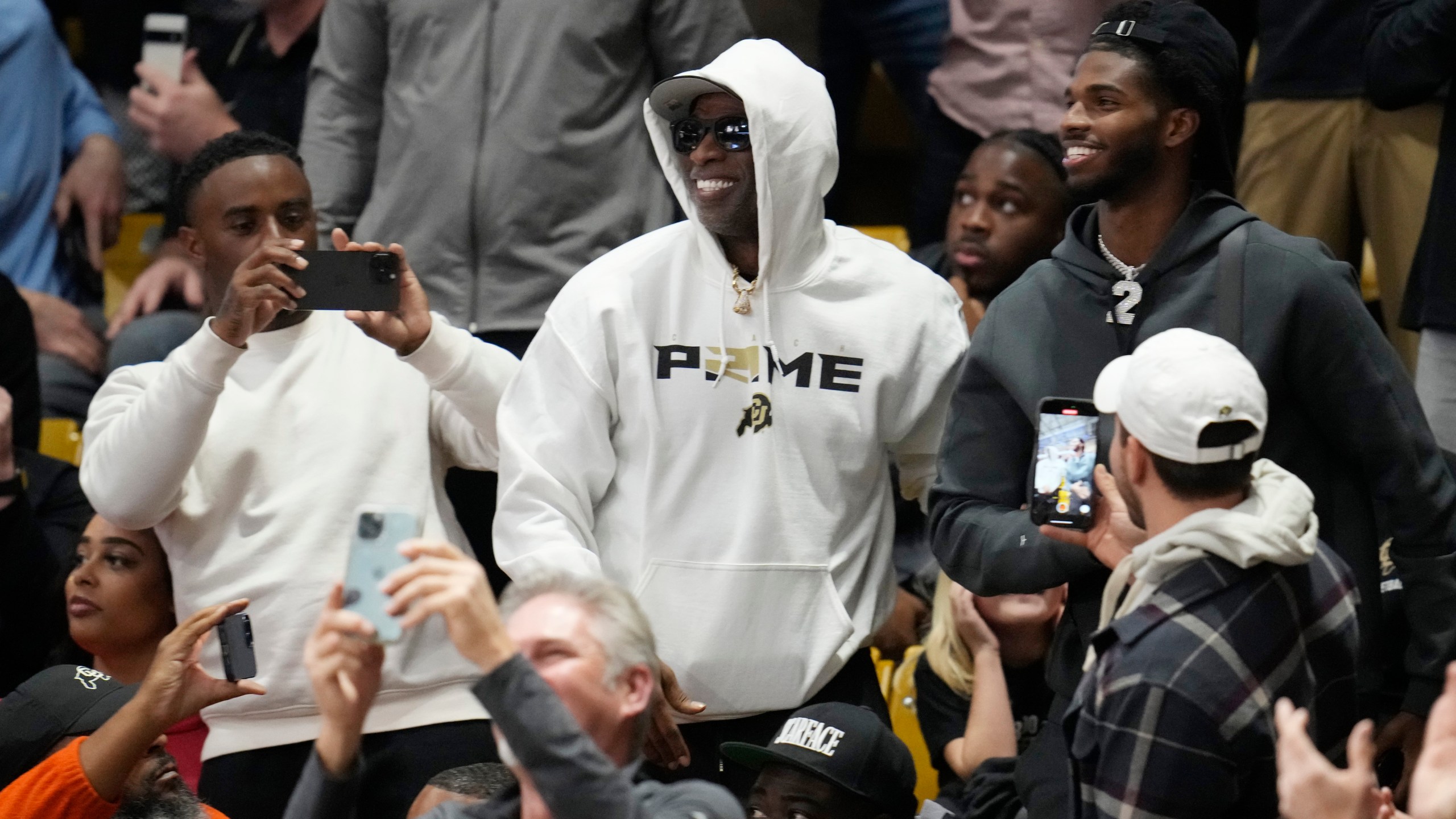 Colorado football coach Deion Sanders, center , and his son, Shedeur, right, greet fans during the second half of an NCAA college basketball game between Colorado and Colorado State