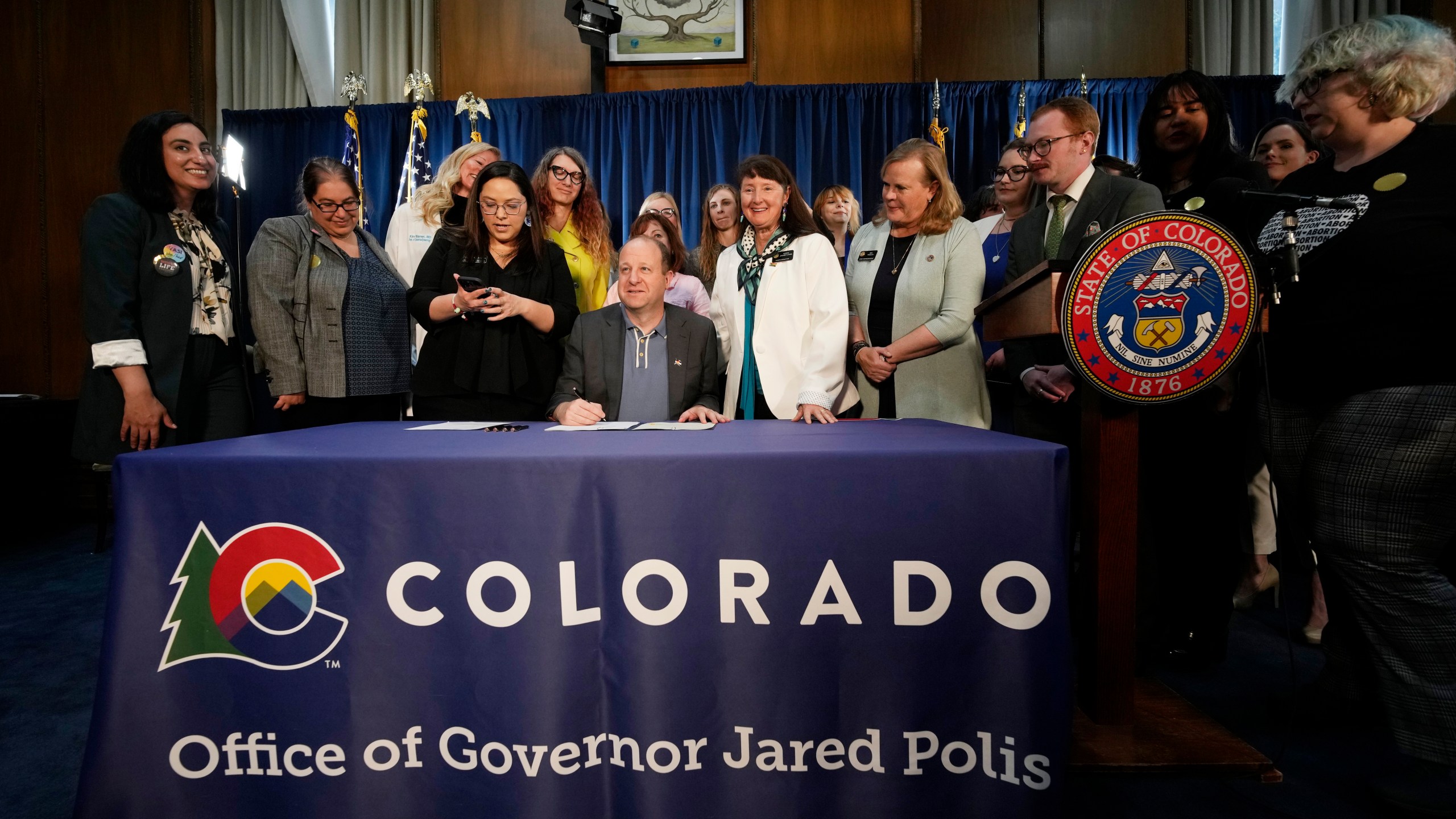 Gov. Jared Polis, center, signs three bills that enshrine protections for abortion and gender-affirming care procedures and medications during a ceremony with bill sponsors and supporters on April 14, 2023, in the State Capitol