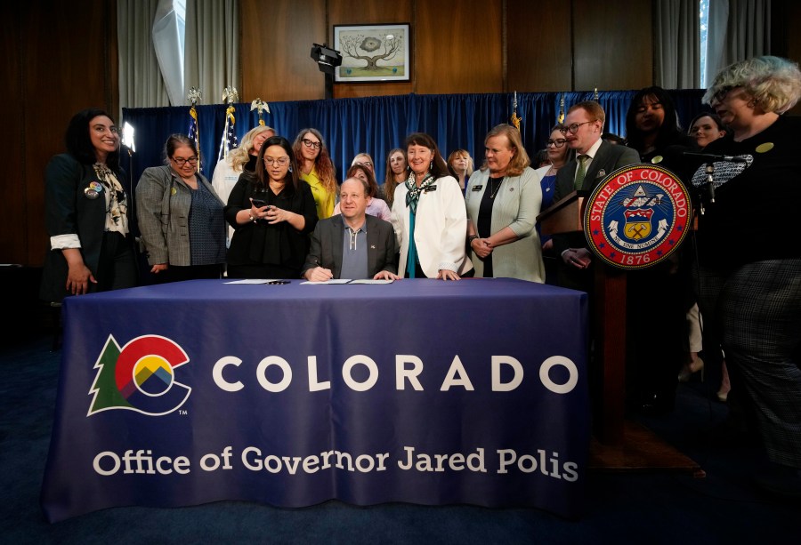 Gov. Jared Polis, center, signs three bills that enshrine protections for abortion and gender-affirming care procedures and medications during a ceremony with bill sponsors and supporters on April 14, 2023, in the State Capitol