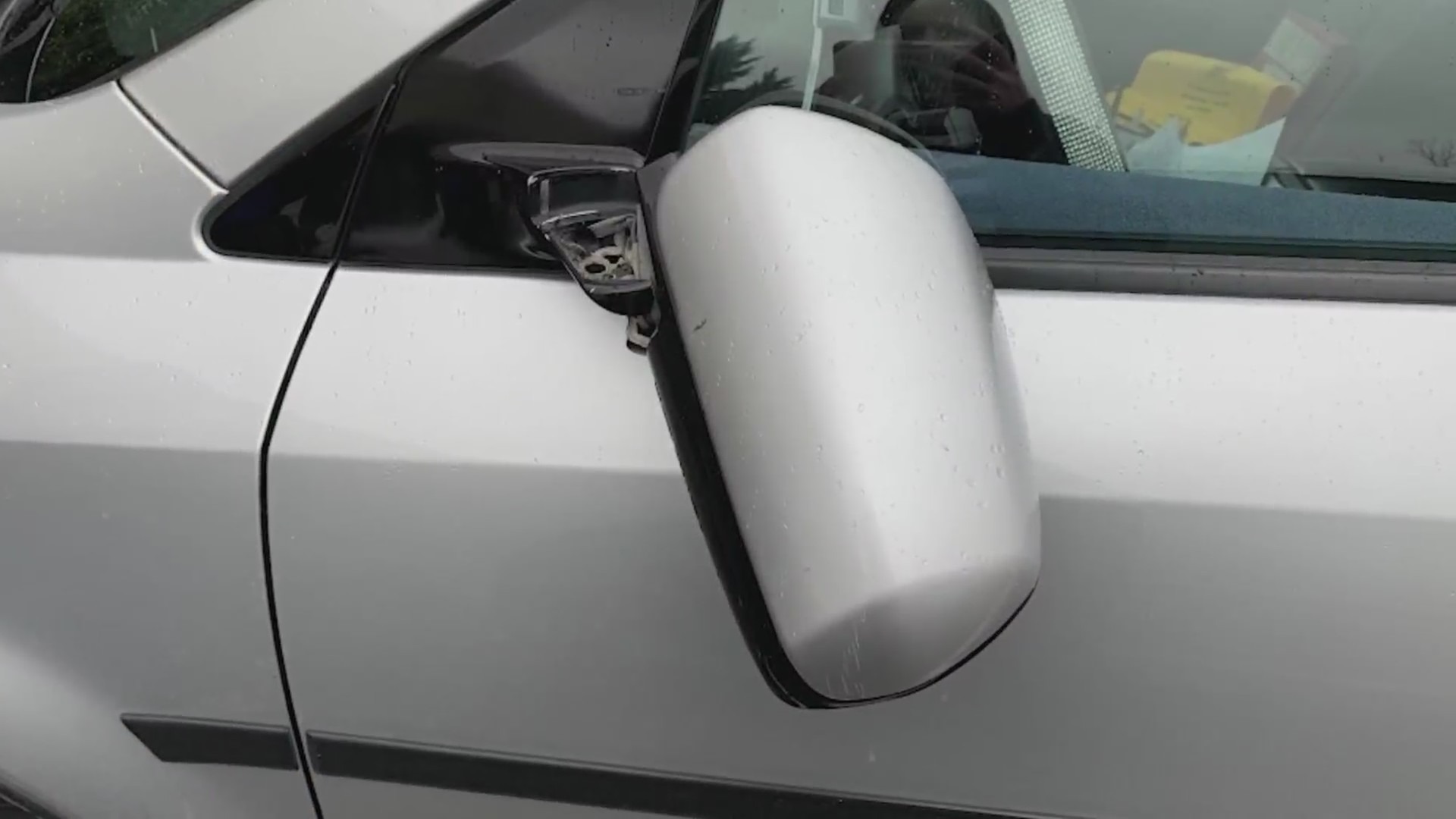 A driver's side rearview mirror hangs broken off the side of a silver car