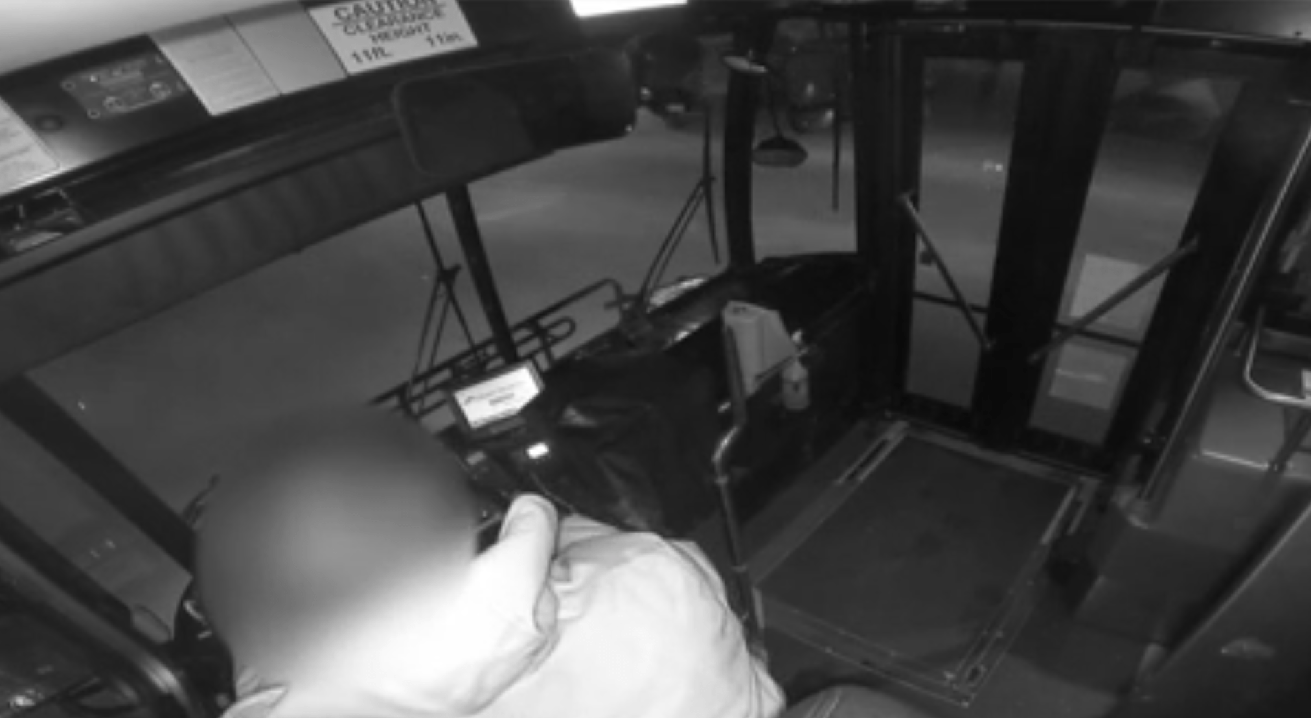 Screen grab of black-and-white surveillance video inside of a bus overlooking a bus driver