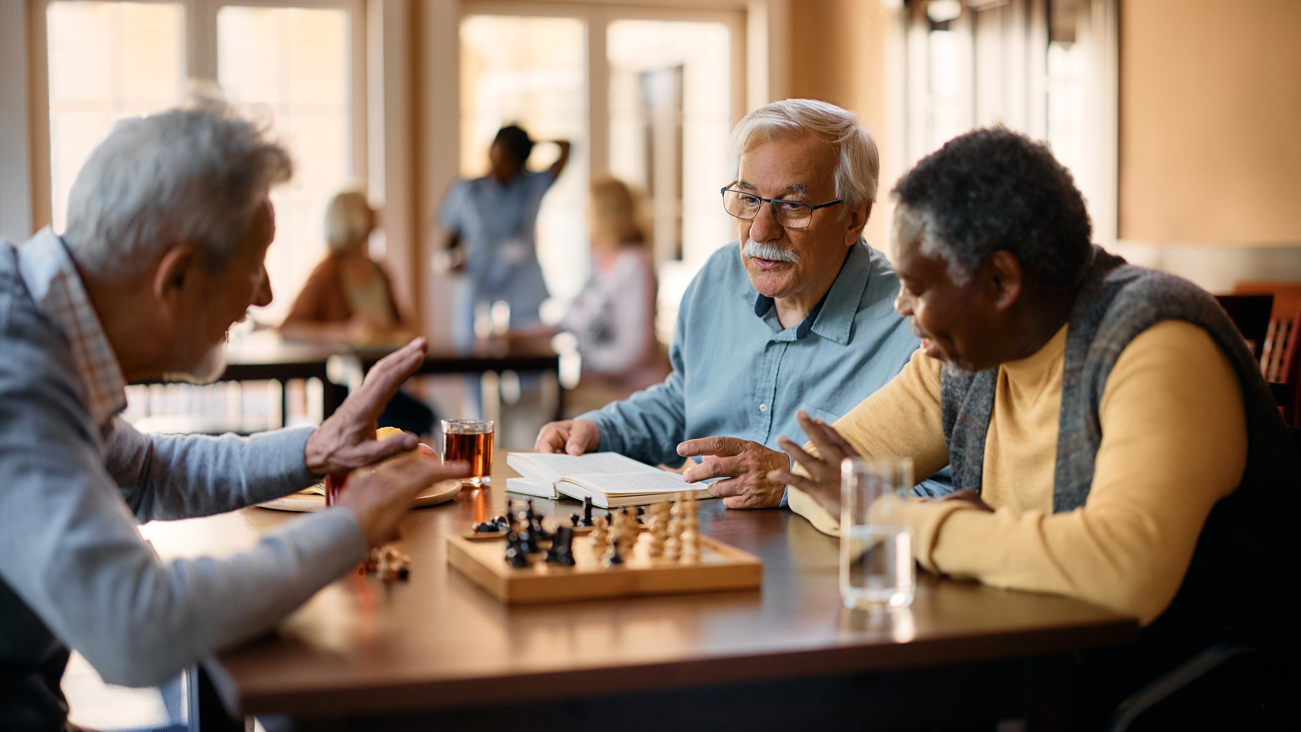 Senior man talking to his friends who are playing chess at nursing home.