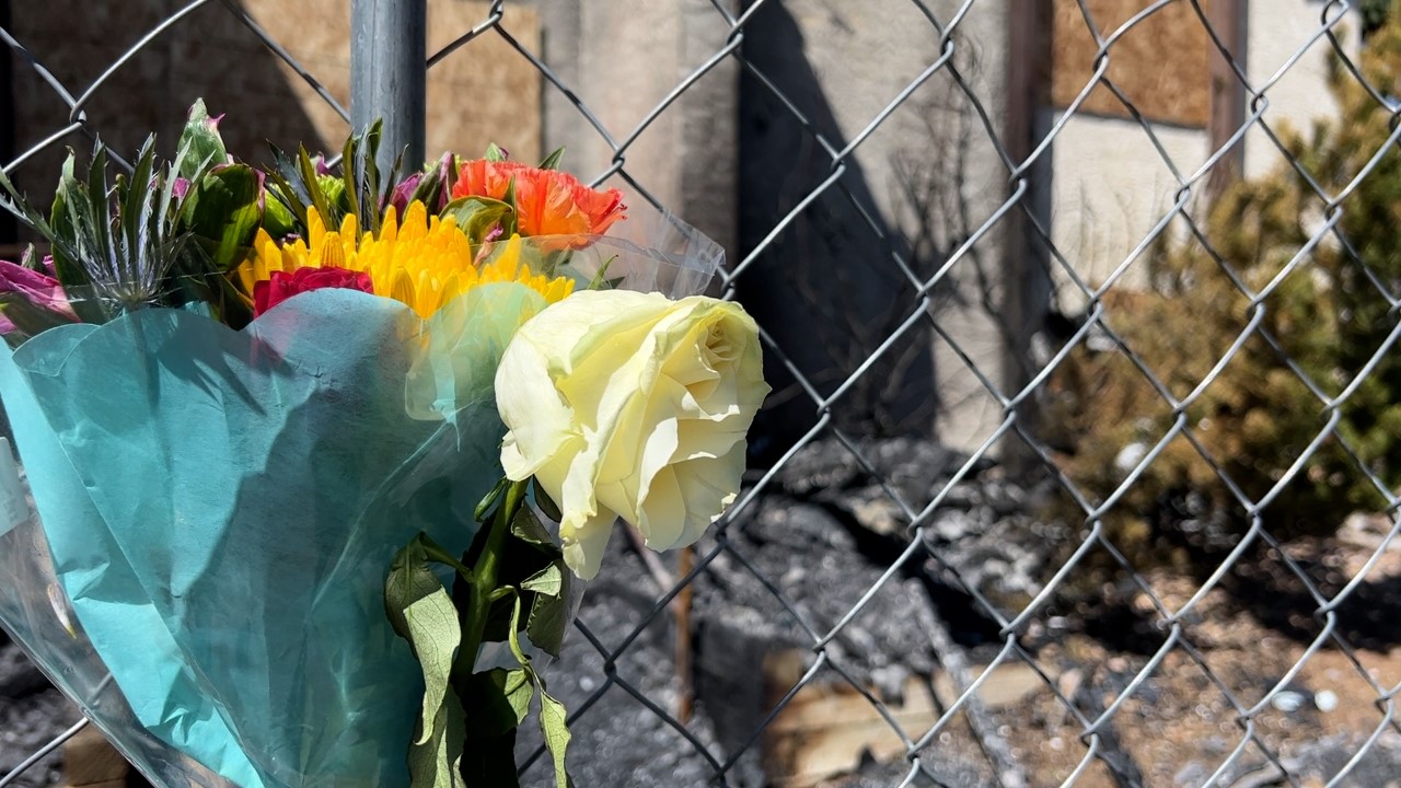 A memorial of flowers along a fence after a deadly fire at Ivy Crossing Apartments