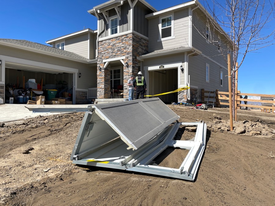 A broken garage door on the ground, several feet in front of a two-story home with no garage door