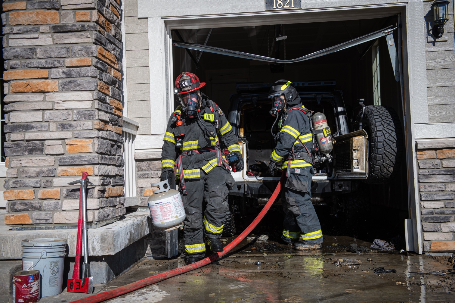 Firefighters in front of a damaged garage with a damaged Jeep Wrangler inside and water all over the ground