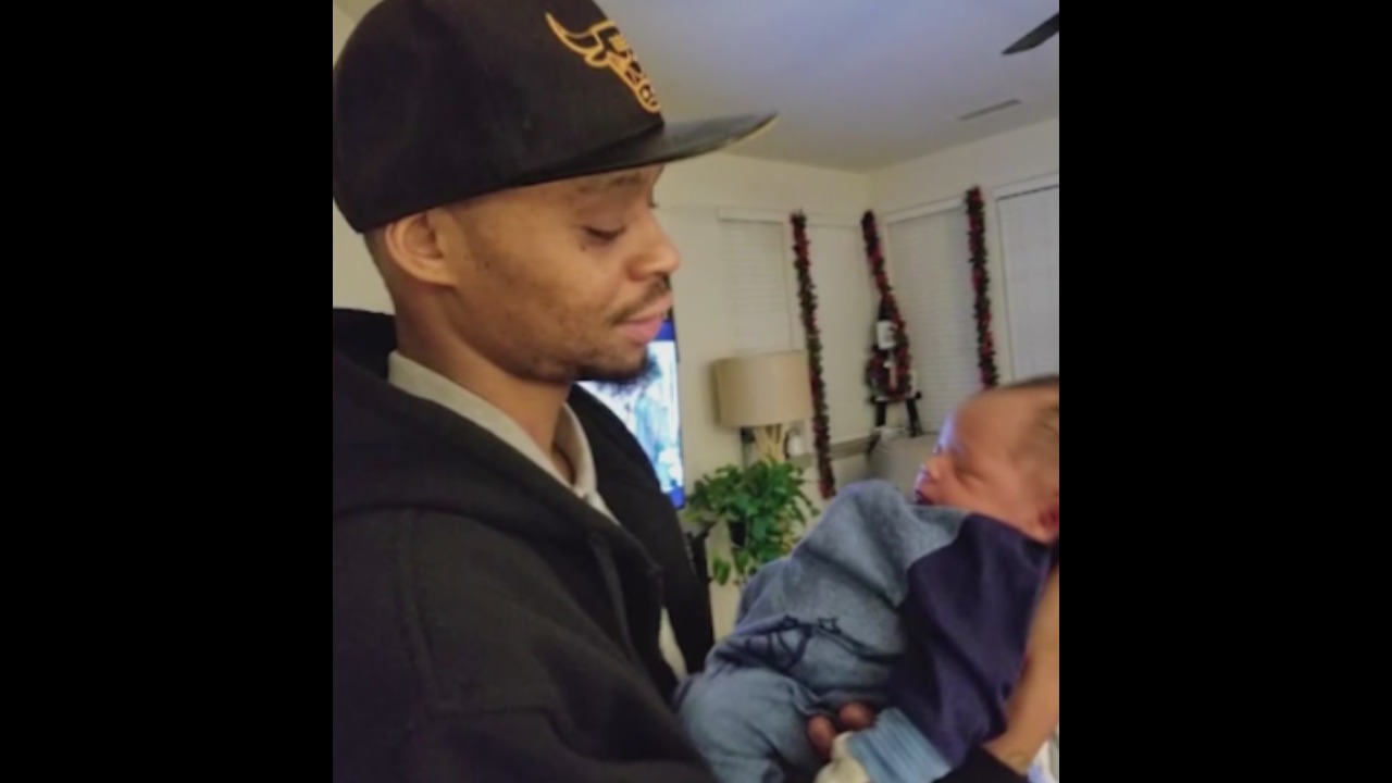 Mar-Shun Cox looks down at a newborn baby in his arms