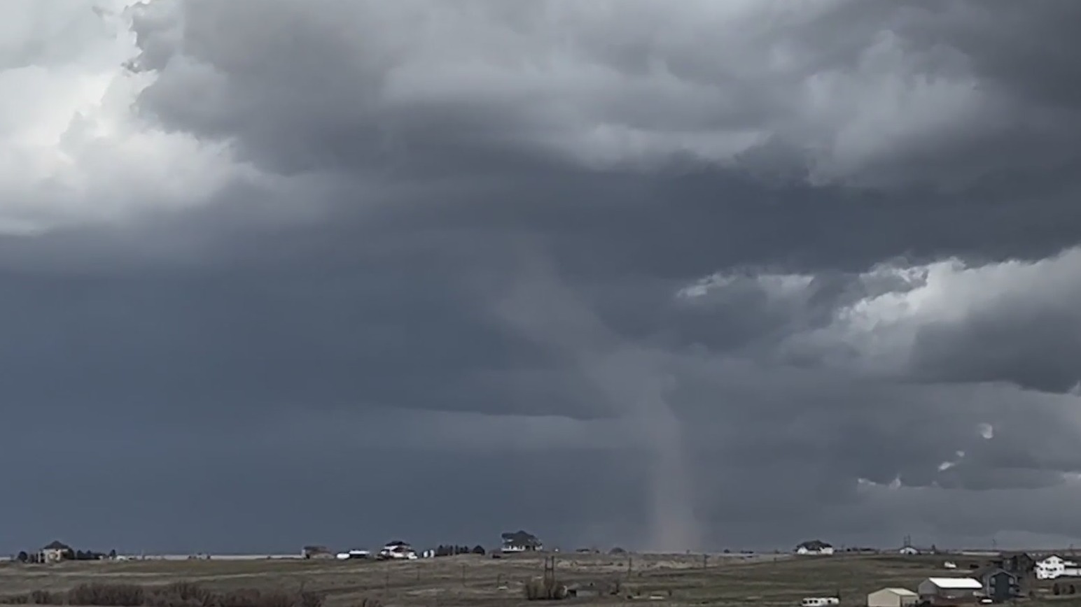 A landspout touches the ground below dark storm clouds over the Colorado plains