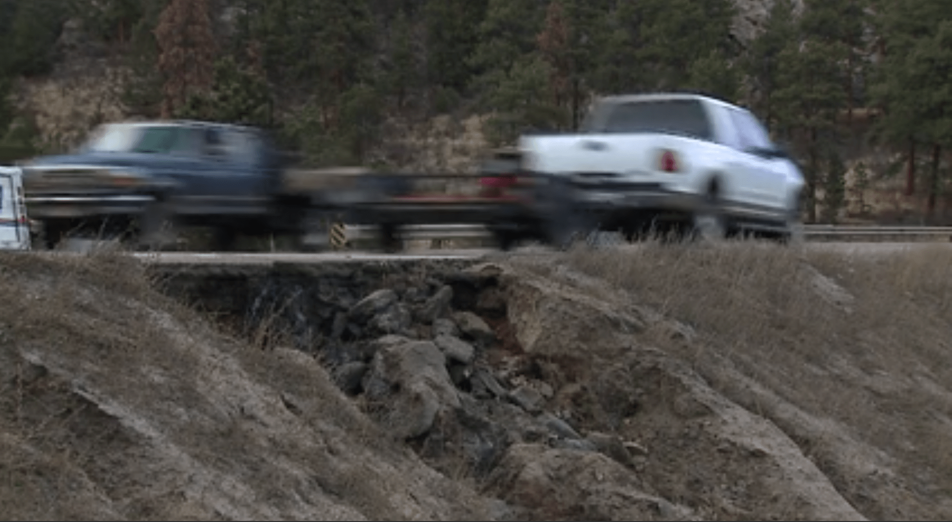 Pick-up trucks travel on both directions of US 285 over an apparently eroding stretch of the highway beneath it