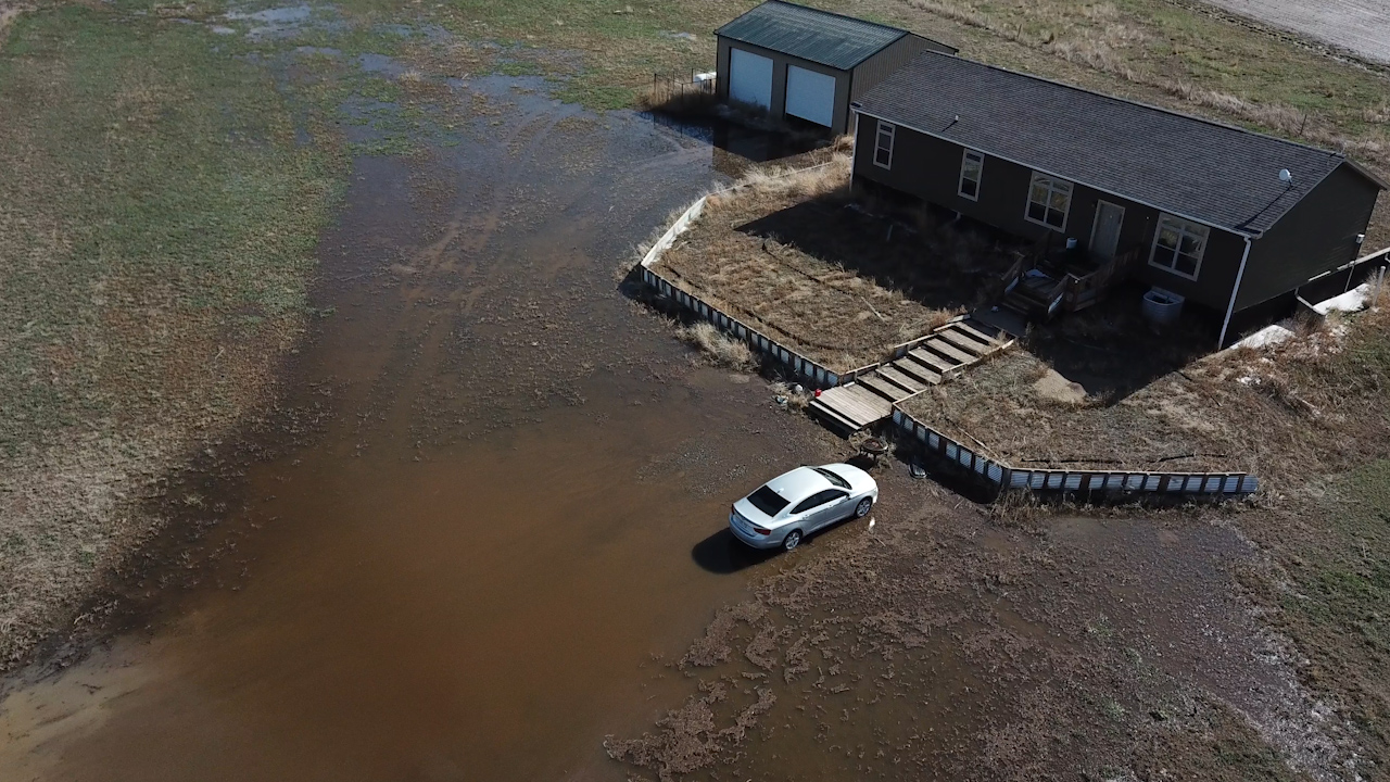 Drone shot of mud and water surrounding a home in a field