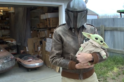 A person dressed in a "Star Wars"-style costume and holding a doll of Grogu, or "Baby Yoda"