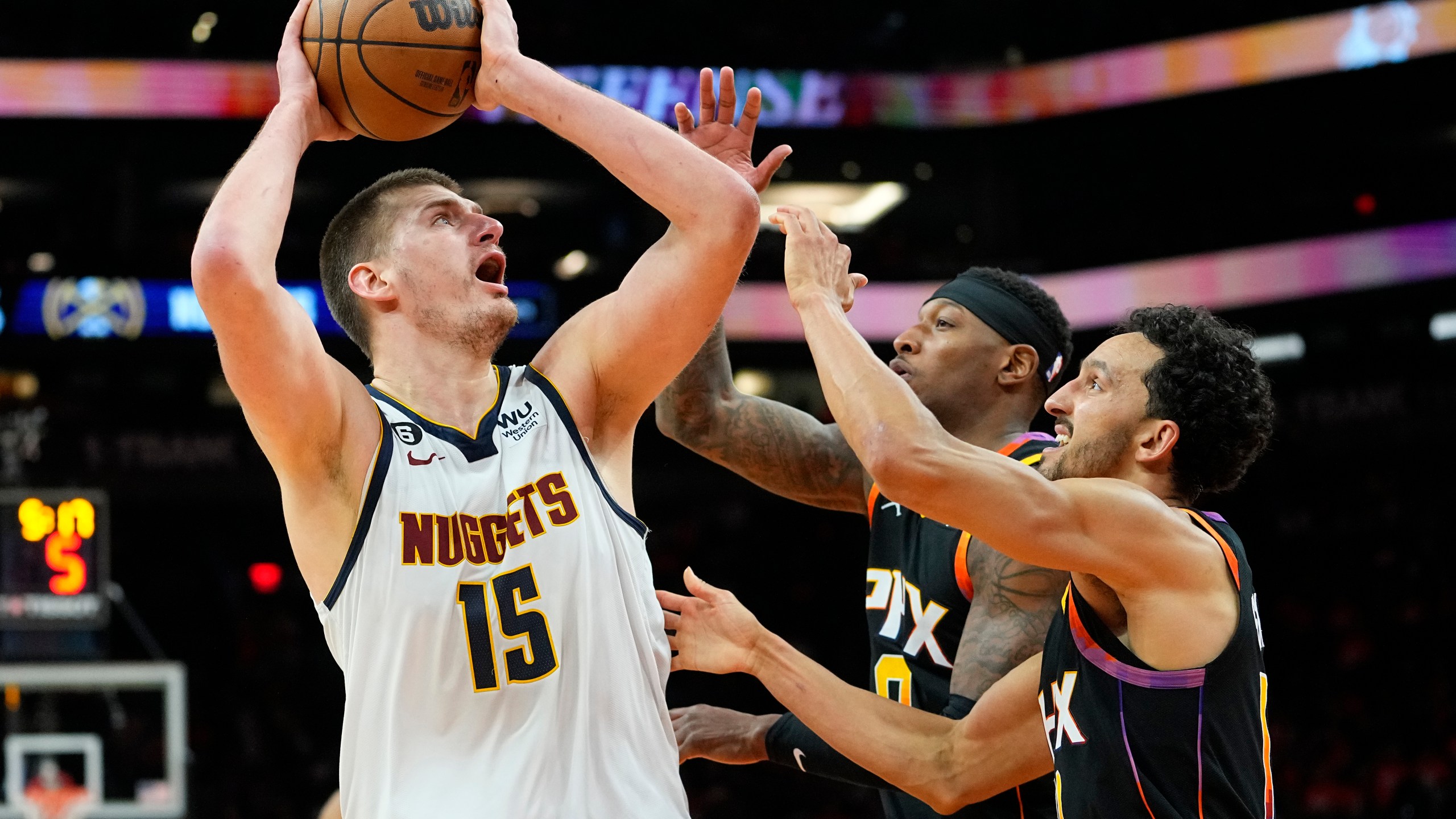 Denver Nuggets center Nikola Jokic (15) shoot over Phoenix Suns guard Landry Shamet, right, and forward Torrey Craig, center, during the second half of Game 6 of an NBA basketball Western Conference semifinal game, Thursday, May 11, 2023, in Phoenix. The Nuggets eliminated the Sun in their 125-100 win. (AP Photo/Matt York)