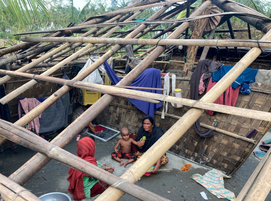 FILE- A family rests inside their home damaged by Cyclone Mocha at Saint Martin island in Cox's Bazar, Bangladesh, Monday, May 15, 2023. Early warnings from weather agencies and preparedness by local governments and aid agencies likely saved thousands of lives from a power Cyclone in that might have been claimed by the cyclone that slammed into the joint coastline of Bangladesh and Myanmar on Sunday. But there are concerns over the large number of people still unaccounted for in regions where preventative action was lacking. (AP Photo/Al-emrun Garjon, File)