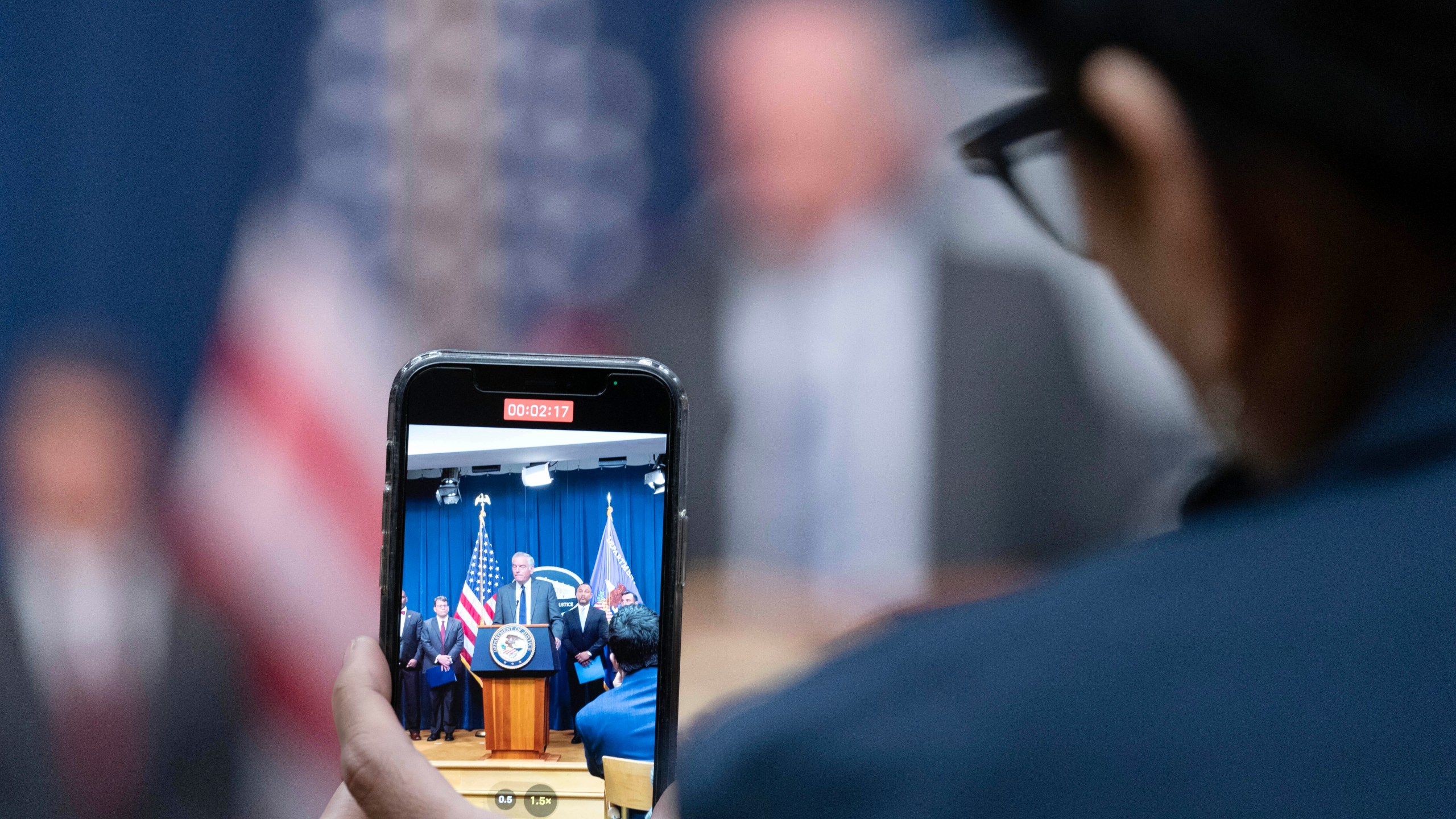 Assistant Secretary for Export Enforcement Matthew Axelrod of the U.S. Commerce Department, is seen on cell phone as he speaks during a news conference at the Department of Justice in Washington, Tuesday, May 16, 2023. (AP Photo/Jose Luis Magana)