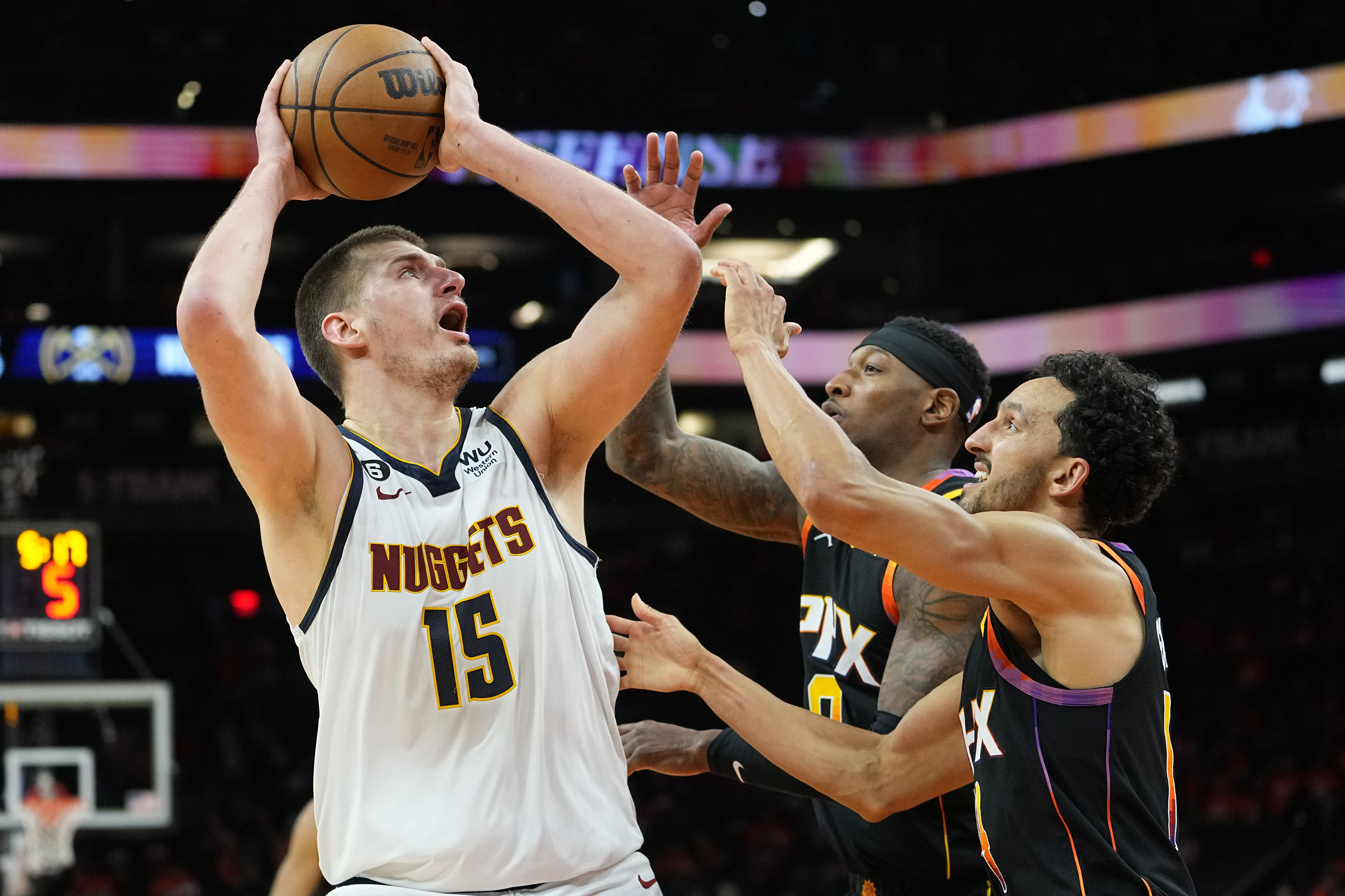 Denver Nuggets center Nikola Jokic (15) shoot over Phoenix Suns guard Landry Shamet, right, and forward Torrey Craig, center, during a game