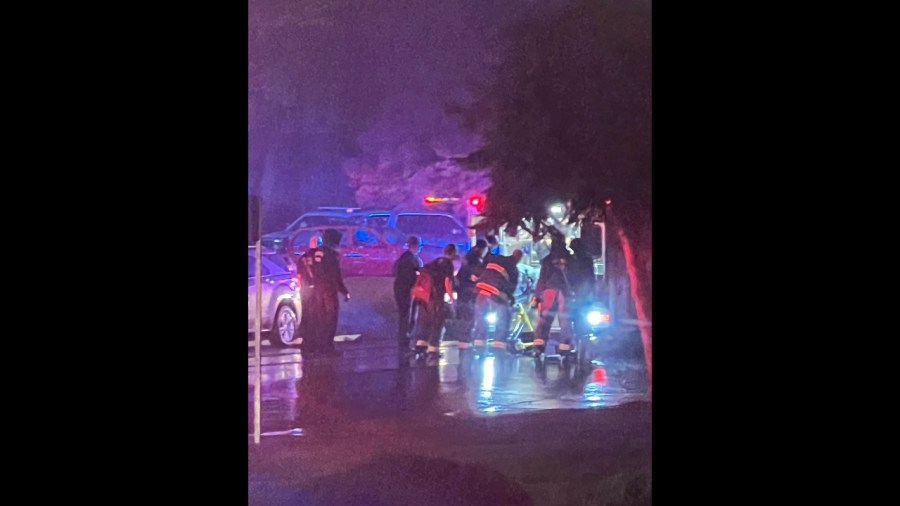 First responders load a patient into an ambulance with red and blue emergency lights lighting up the scene at night