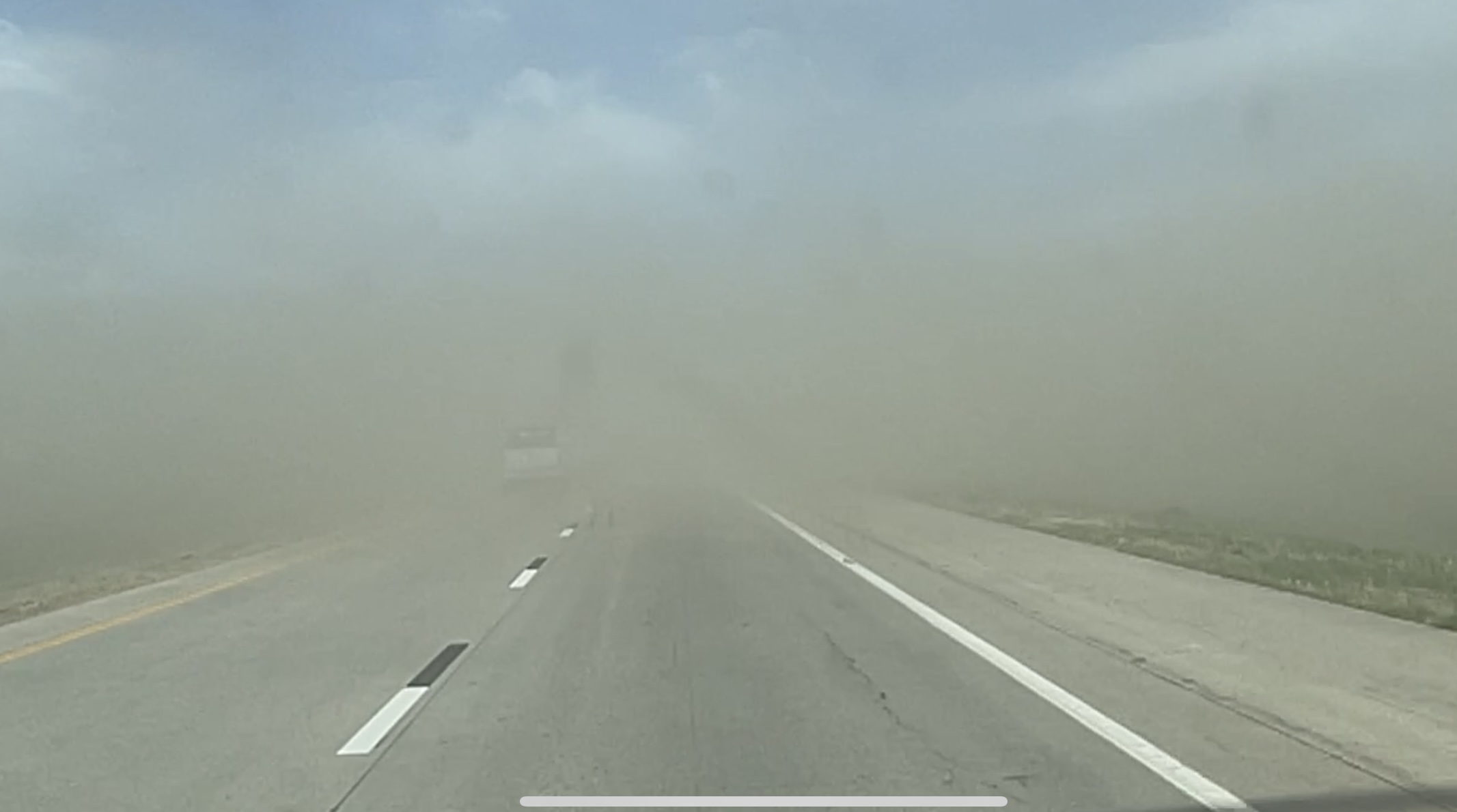 Dust covers a highway in daylight, with a vehicle ahead nearly obscured by the brownout