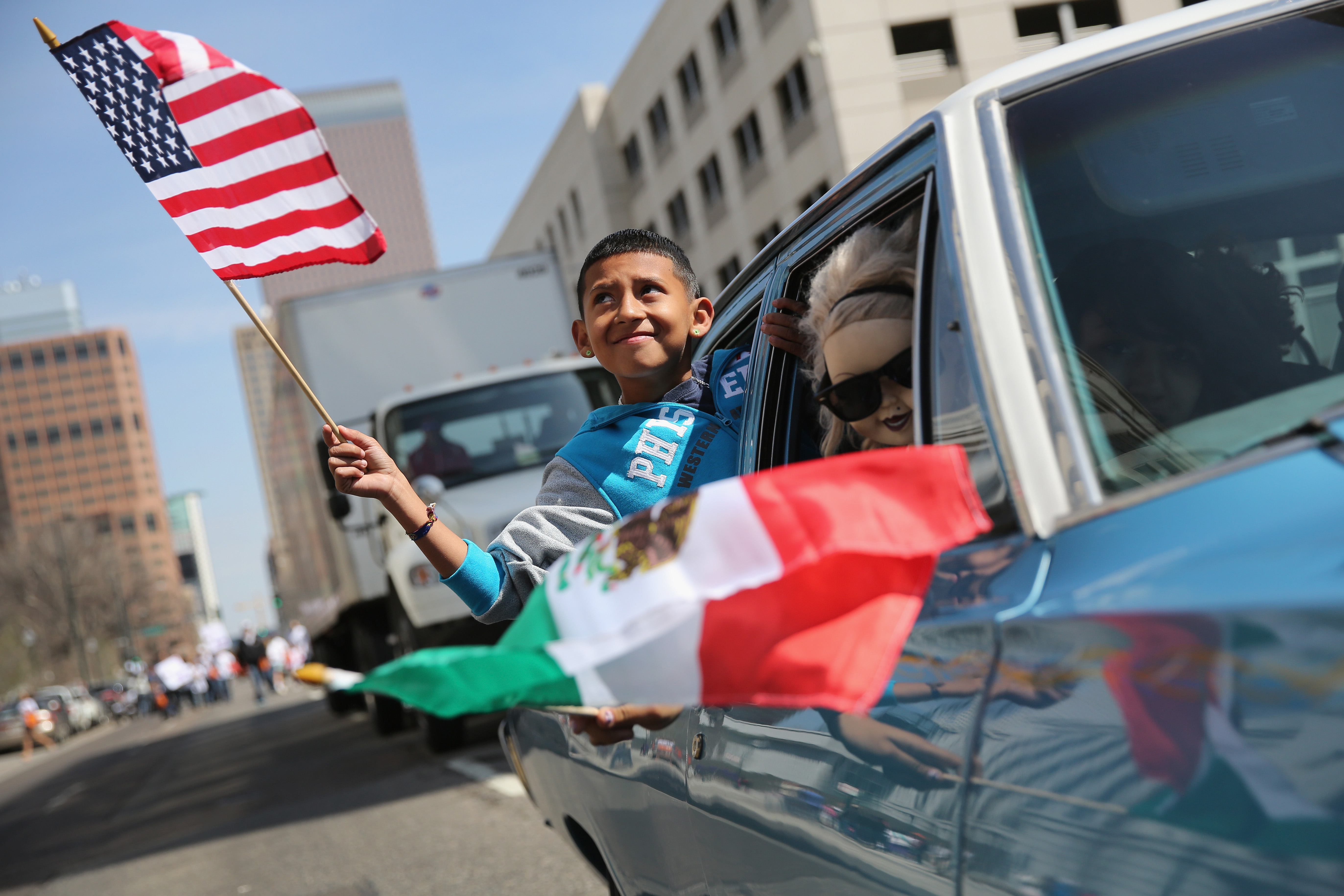 A boy rides in a low rider with a Mexico flag hanging out the window while he holds a U.S. flag during a Cinco de Mayo parade