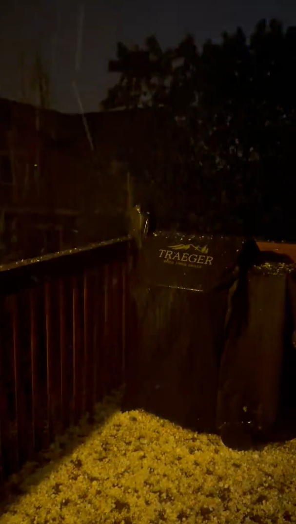 Hail piled up around a grill on a patio at night