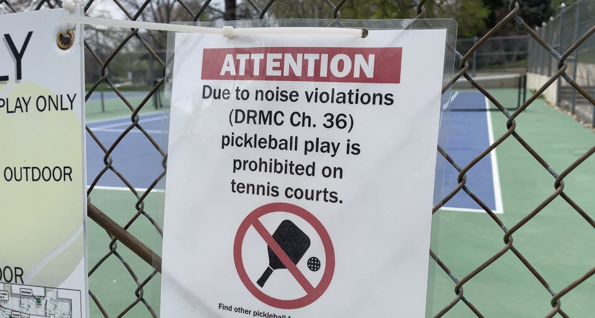 A sign prohibiting pickleball because of noise violations is posted on chain-link fence outside of a court.