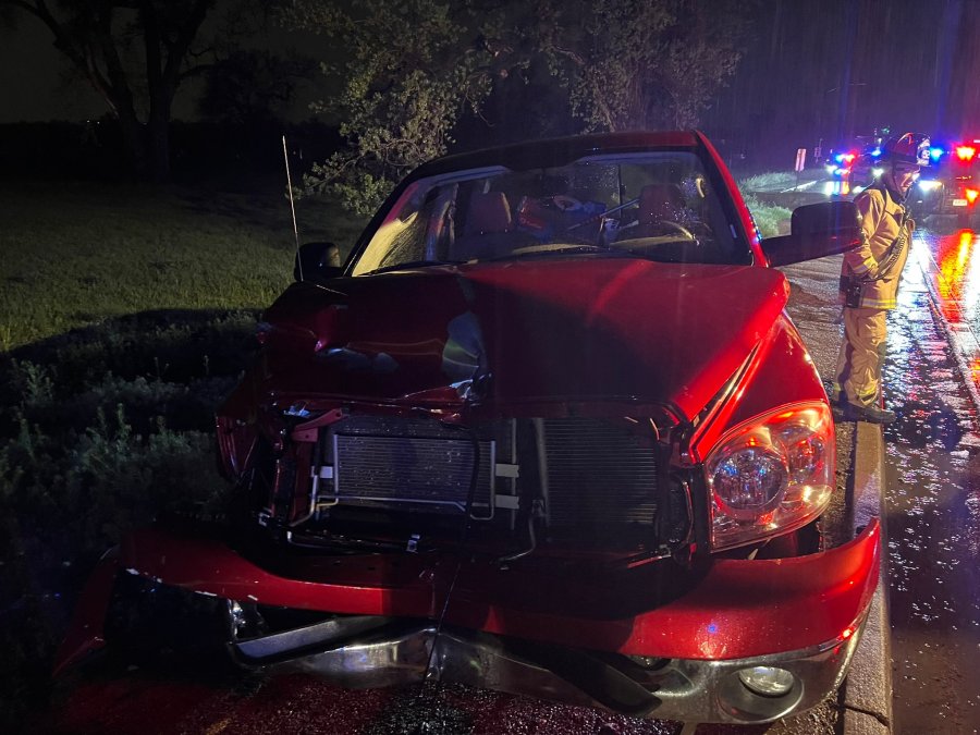 A red truck has damage to the front end with emergency responders nearby.