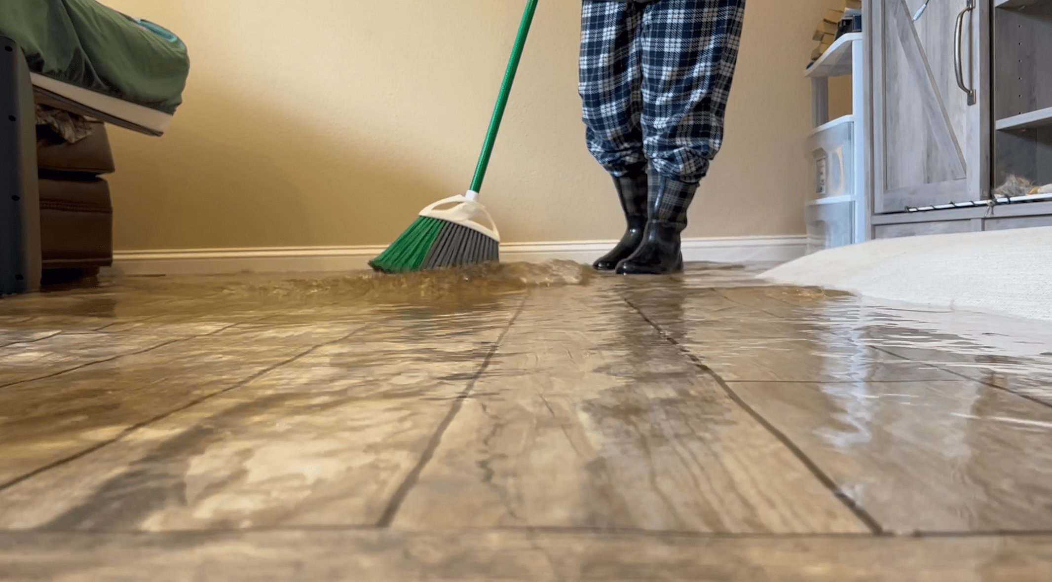 A low-angle image of someone using a broom to move an inch of water on a floor